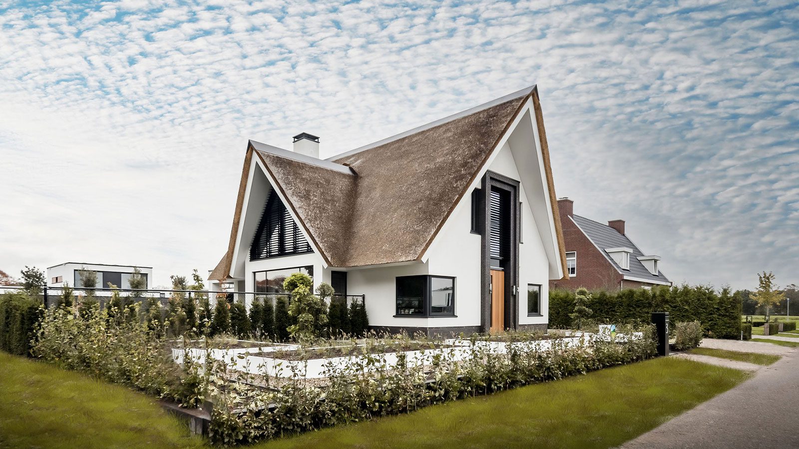 Voorzijde rietgedekte villa, zwarte kozijnen, houten deuren.